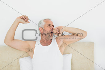 Mature man stretching arms in bed