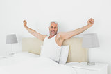 Mature smiling man stretching his arms in bed