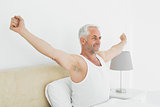 Mature smiling man stretching his arms in bed