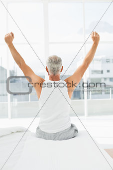 Rear view of mature man stretching arms in bed