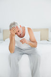Thoughtful mature man yawning sitting in bed