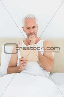 Relaxed mature man reading book in bed