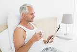 Mature man with coffee cup and newspaper in bed