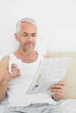 Mature man with coffee cup and newspaper in bed