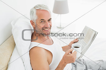 Smiling mature man with coffee cup and newspaper in bed