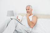 Man with coffee cup reading newspaper in bed
