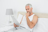 Mature man reading newspaper in bed at home