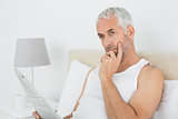 Casual thoughtful mature man with newspaper in bed