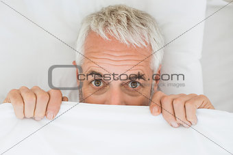 Mature shocked man covering face with sheet in bed