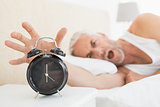 Blurred mature man extending hand to alarm clock