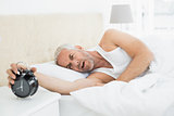 Mature man extending hand to alarm clock in bed