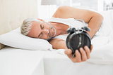 Sleepy mature man holding alarm clock in bed