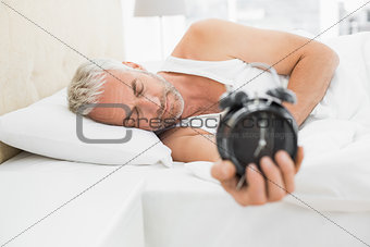 Sleepy mature man holding alarm clock in bed