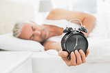 Mature man holding out alarm clock in bed