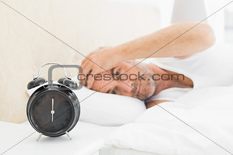 Man resting in bed with alarm clock in foreground