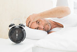 Man resting in bed with alarm clock in foreground