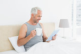 Smiling mature man with digital tablet and coffee table in bed