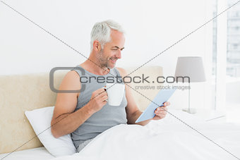 Smiling mature man with digital tablet and coffee table in bed