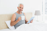 Mature man with digital tablet and coffee table in bed