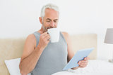 Man with digital tablet drinking coffee in bed