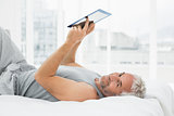 Smiling mature man resting with digital tablet in bed