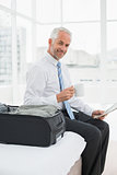 Portrait of a businessman with coffee cup reading newspaper by luggage