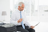 Businessman with coffee cup reading newspaper by luggage