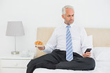 Businessman text messaging while holding croissant in bed