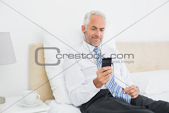 Businessman listening music with his phone in bed