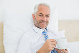 Smiling businessman with a cup of tea in bed