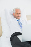 Mature businessman looking at laptop in bed