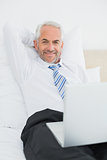 Relaxed mature businessman with laptop in bed