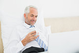 Smiling mature businessman using laptop in bed