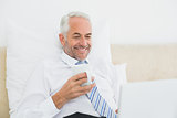 Businessman using laptop while having coffee in bed