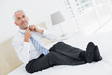 Mature businessman adjusting neck tie in bed