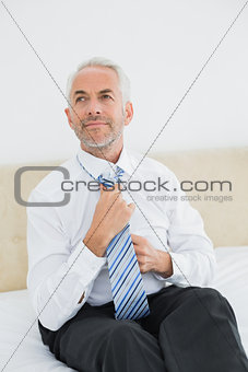 Thoughtful businessman adjusting neck tie in bed