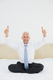 Happy mature businessman gesturing thumbs up on bed