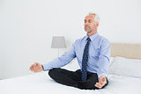 Relaxed mature businessman sitting in lotus posture on bed