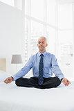 Relaxed mature businessman sitting in lotus posture on bed