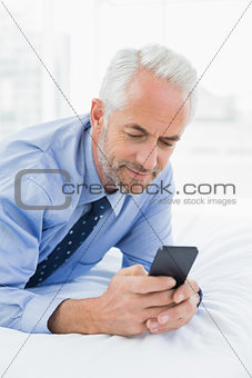 Relaxed businessman text messaging in bed