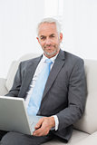 Mature businessman with laptop sitting on sofa