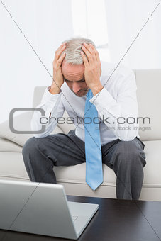 Worried mature businessman with laptop at home