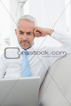 Mature businessman using laptop on sofa in living room