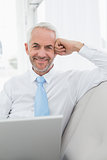 Smiling mature businessman using laptop on sofa in living room