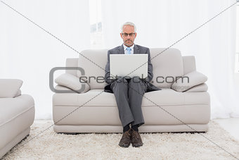 Concentrated businessman using laptop on sofa in living room