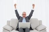 Elegant businessman cheering in front of laptop at home