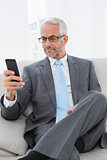 Elegant mature businessman text messaging on sofa