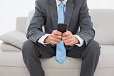 Mid section of a well dressed man text messaging on sofa
