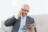 Businessman with cellphone and newspaper at home