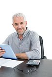 Mature businessman with digital tablet and calculator at desk